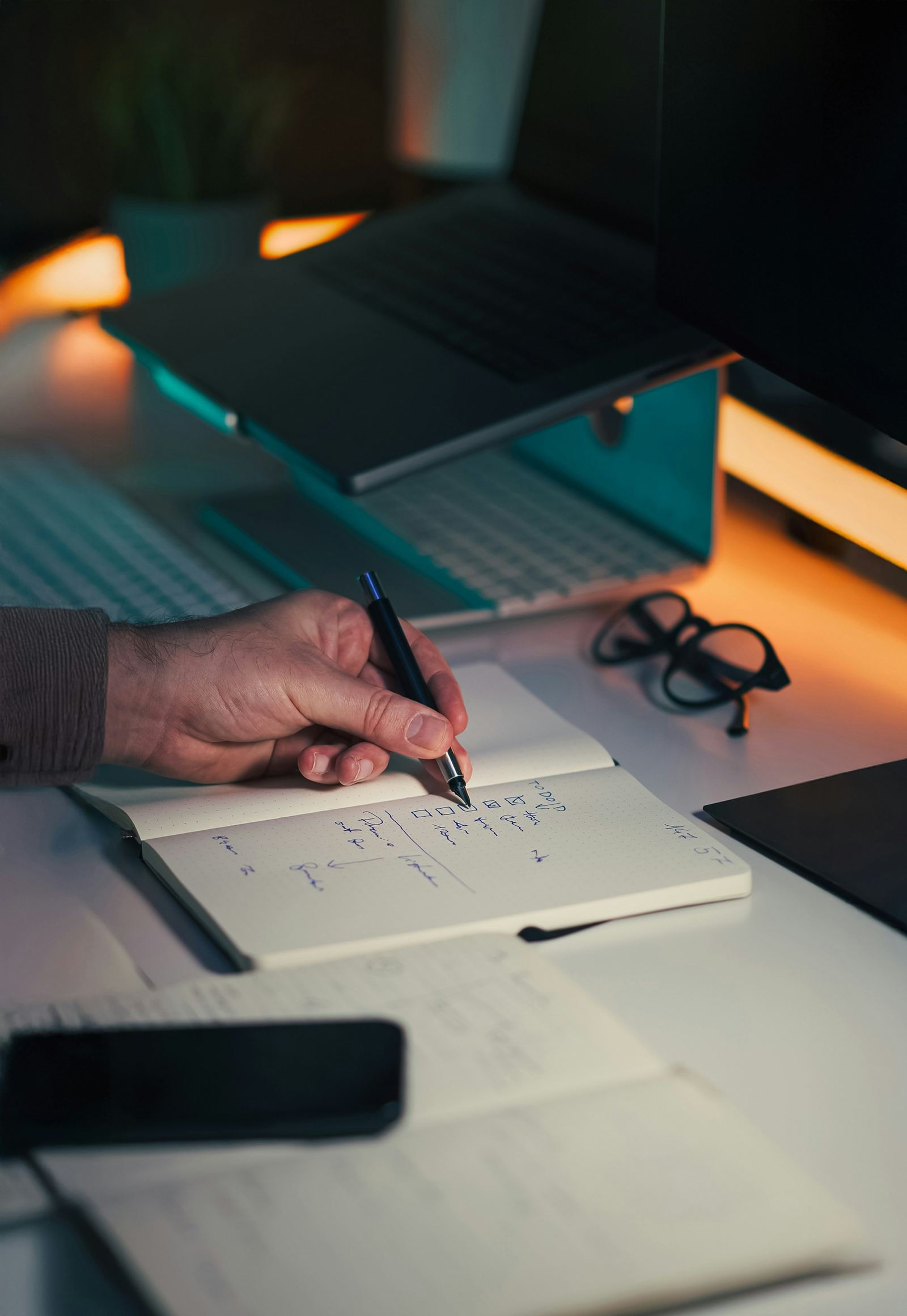 Hands writing research notes at a desk beside a laptop