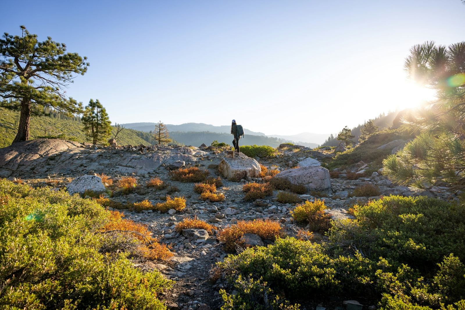 A hiker seen from behind on a mountain path at sunrise